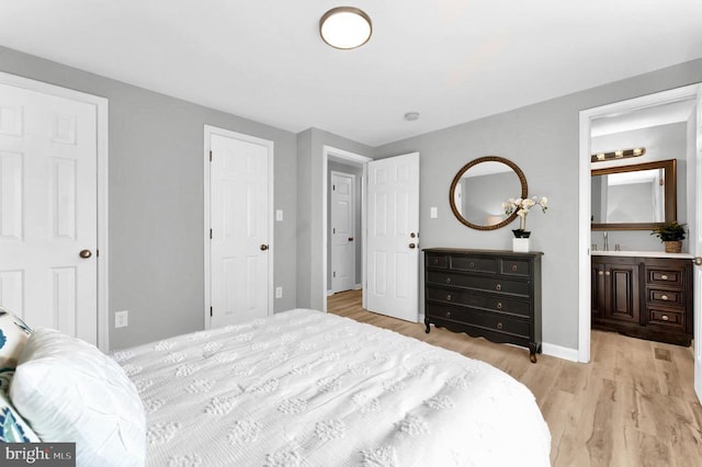 bedroom with a sink, light wood-style floors, baseboards, and connected bathroom