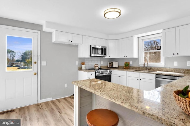 kitchen with light stone counters, white cabinetry, stainless steel appliances, and a sink