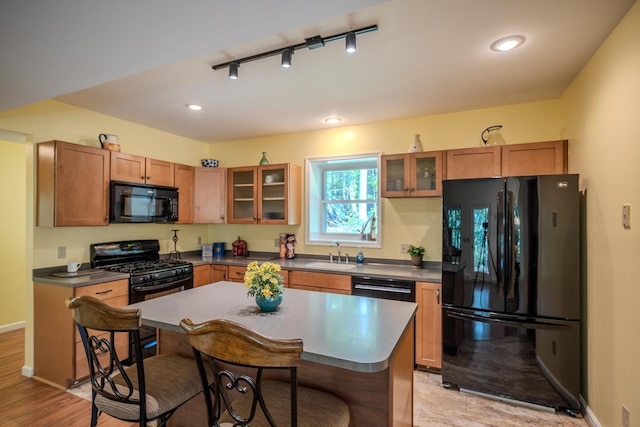 kitchen with black appliances, a sink, a kitchen breakfast bar, glass insert cabinets, and recessed lighting