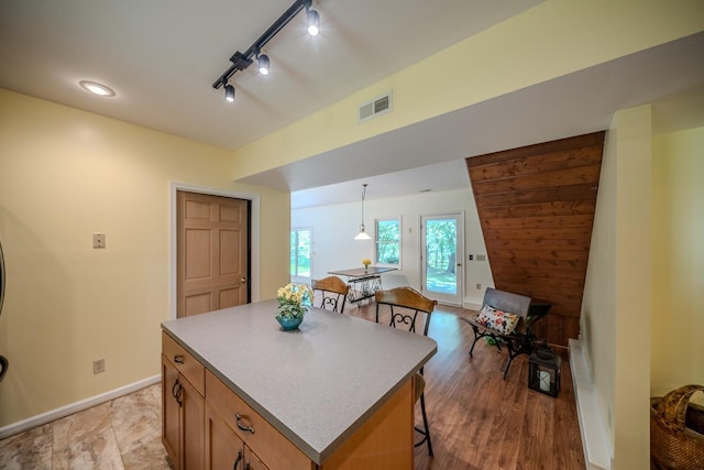 kitchen featuring a kitchen bar, a center island, baseboards, rail lighting, and brown cabinetry