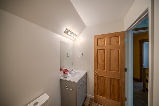 half bath featuring vanity, lofted ceiling, and toilet