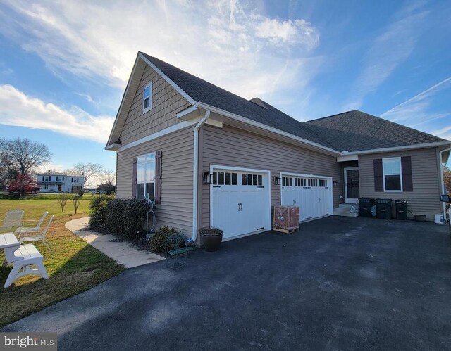 view of side of home with driveway, a garage, a shingled roof, and a lawn