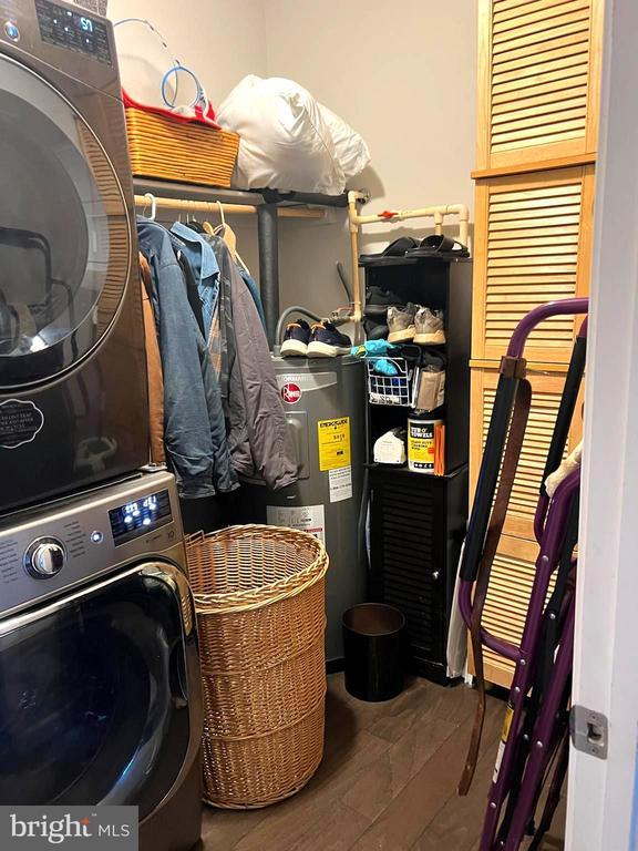 laundry room featuring stacked washer / dryer, water heater, and wood finished floors