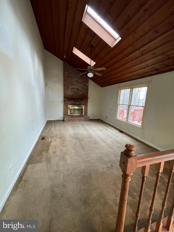 unfurnished living room featuring a brick fireplace, wood ceiling, and carpet