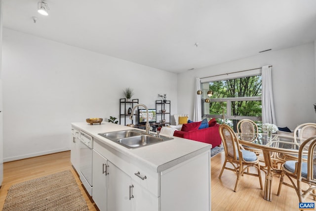 kitchen featuring a sink, dishwasher, light wood-style floors, light countertops, and white cabinets