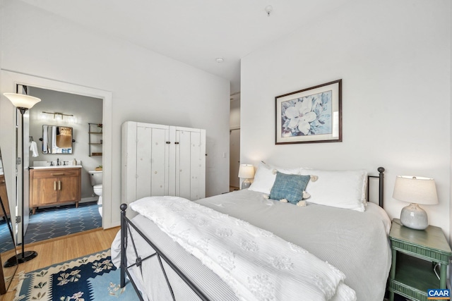 bedroom featuring wood finished floors, ensuite bathroom, and a sink