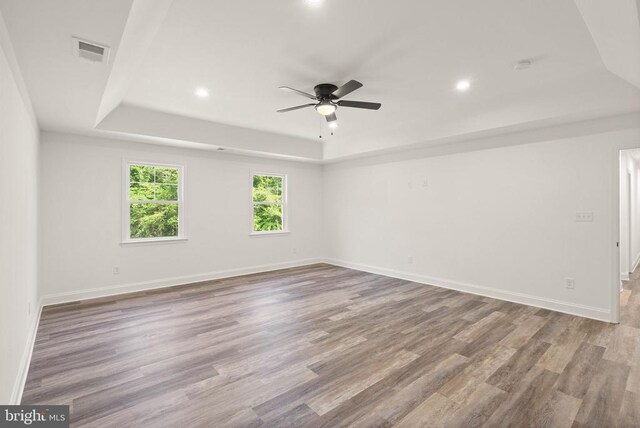  - empty room with a raised ceiling, a ceiling fan, recessed lighting, wood finished floors, and a smoke detector