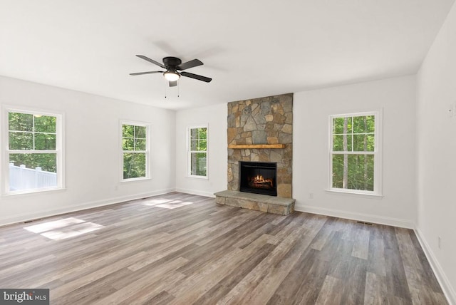  - unfurnished living room with wood finished floors, baseboards, ceiling fan, and a stone fireplace