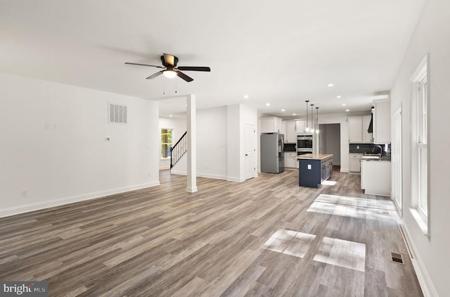  - unfurnished living room featuring light wood-type flooring, a sink, a ceiling fan, stairway, and baseboards