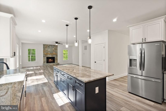  - kitchen featuring stainless steel fridge with ice dispenser, a sink, a stone fireplace, ceiling fan, and white cabinetry