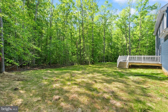  - view of green lawn featuring a wooden deck and a wooded view