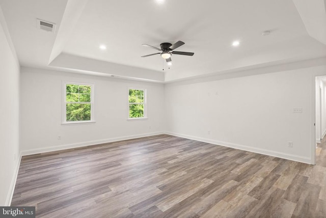  - empty room with a raised ceiling, a ceiling fan, recessed lighting, wood finished floors, and baseboards