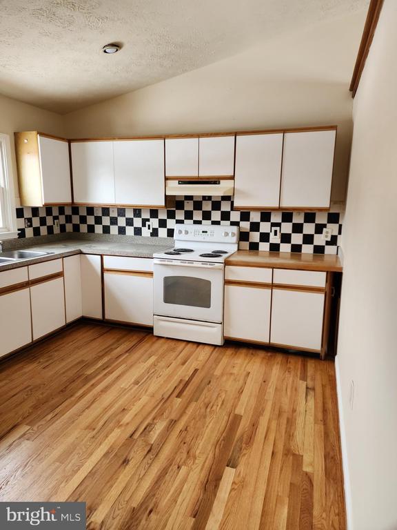  - kitchen with white range with electric stovetop, under cabinet range hood, white cabinets, a textured ceiling, and tasteful backsplash