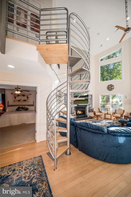 stairs featuring a high ceiling, wood finished floors, a glass covered fireplace, recessed lighting, and ceiling fan