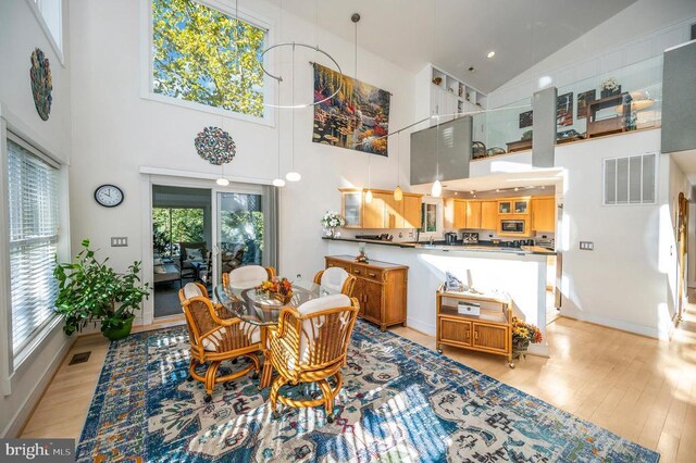 dining area featuring high vaulted ceiling, light wood-style flooring, and baseboards