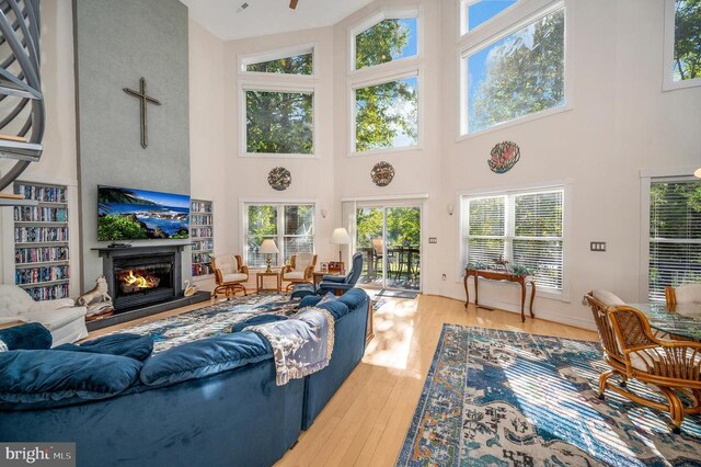 living area with a glass covered fireplace, hardwood / wood-style flooring, a towering ceiling, and healthy amount of natural light