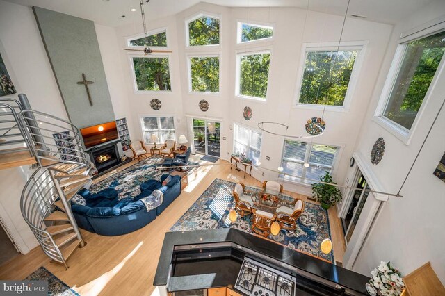 living area with wood finished floors, a towering ceiling, plenty of natural light, and a warm lit fireplace
