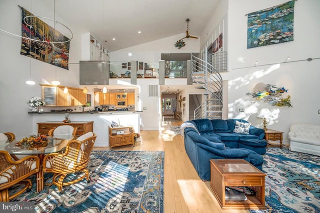 living area with high vaulted ceiling, light wood finished floors, and stairs