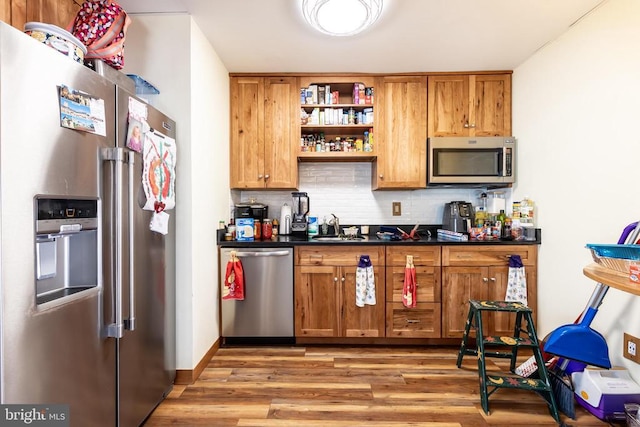 kitchen featuring dark countertops, light wood finished floors, appliances with stainless steel finishes, and brown cabinetry