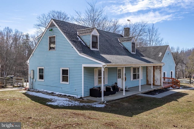 view of front of home with a front yard, covered porch, roof with shingles, and a chimney