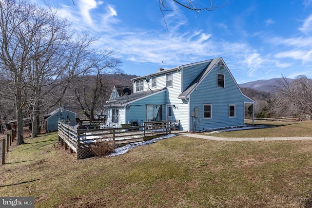 back of property with a deck with mountain view, a chimney, and a lawn