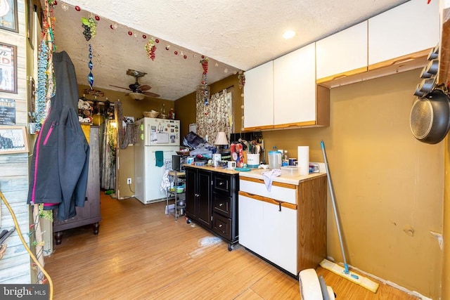 kitchen featuring light countertops, white cabinets, a textured ceiling, light wood-type flooring, and dark cabinetry