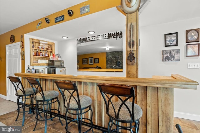 indoor wet bar featuring baseboards and black microwave