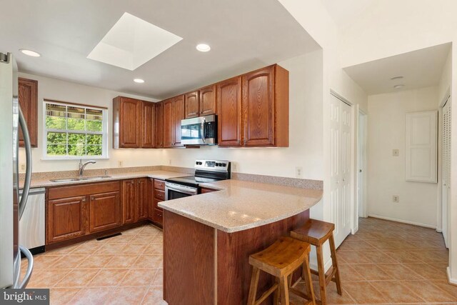  - kitchen featuring stainless steel appliances, a peninsula, a breakfast bar, a skylight, and brown cabinets