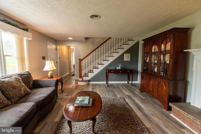 living area with a textured ceiling, wood finished floors, stairs, and baseboards