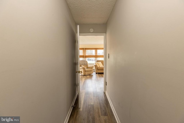 hallway featuring a textured ceiling, dark wood-style floors, and baseboards