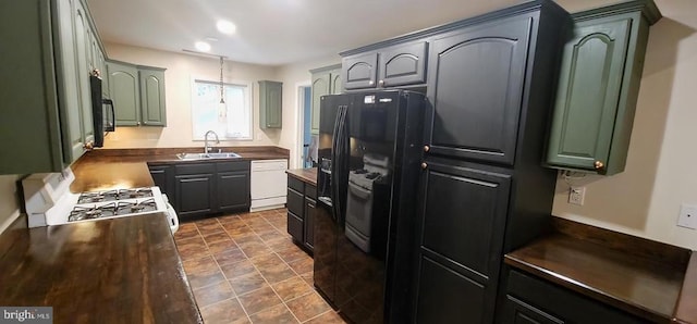 kitchen featuring white appliances, a sink, dark countertops, stone finish flooring, and green cabinetry