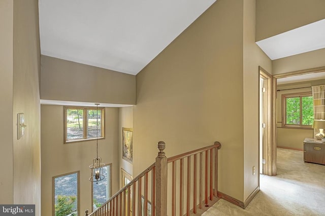 hall with an upstairs landing, carpet, high vaulted ceiling, and baseboards