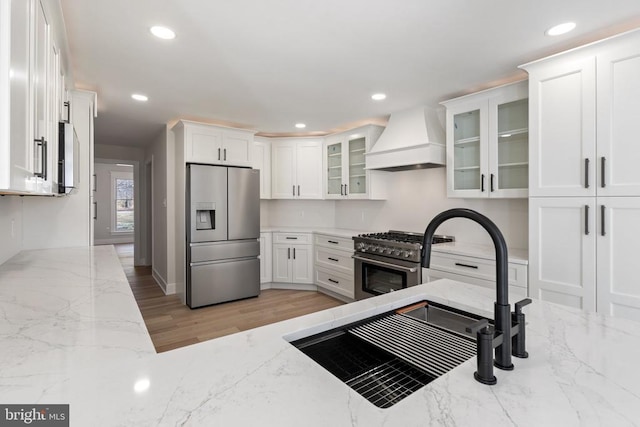 kitchen with white cabinets, light stone countertops, premium range hood, and stainless steel appliances