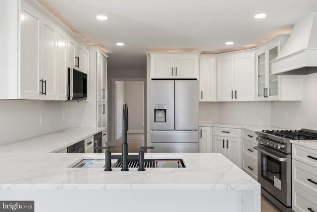 kitchen with a sink, white cabinetry, stainless steel appliances, and premium range hood