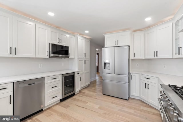 kitchen featuring wine cooler, light countertops, appliances with stainless steel finishes, light wood-style floors, and white cabinets