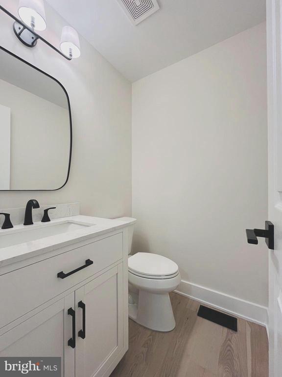 half bath with visible vents, toilet, wood finished floors, baseboards, and vanity