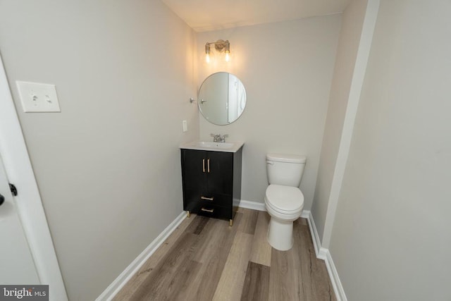  - half bathroom with vanity, toilet, baseboards, and wood finished floors