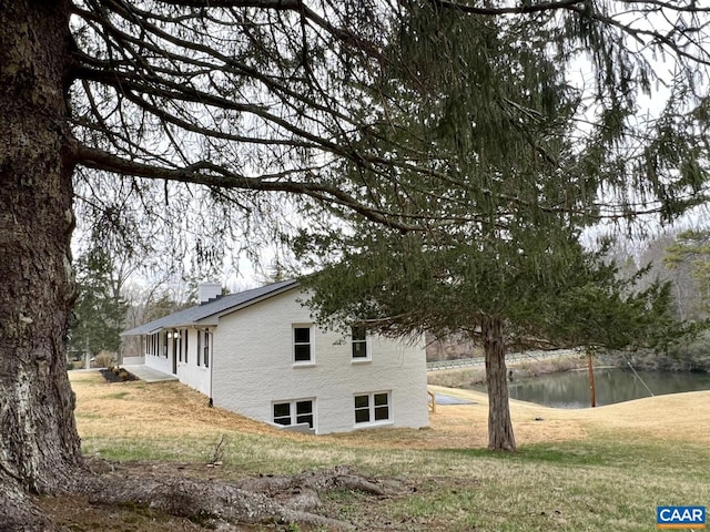 view of home's exterior featuring a yard, a water view, and a chimney