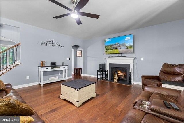  - living room featuring arched walkways, ceiling fan, a glass covered fireplace, stairs, and wood finished floors