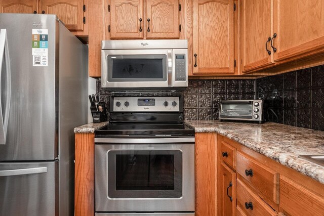 180 Iron Works Ln, Elkton, VA 22827 - kitchen featuring brown cabinets, a toaster, stainless steel appliances, backsplash, and light stone counters