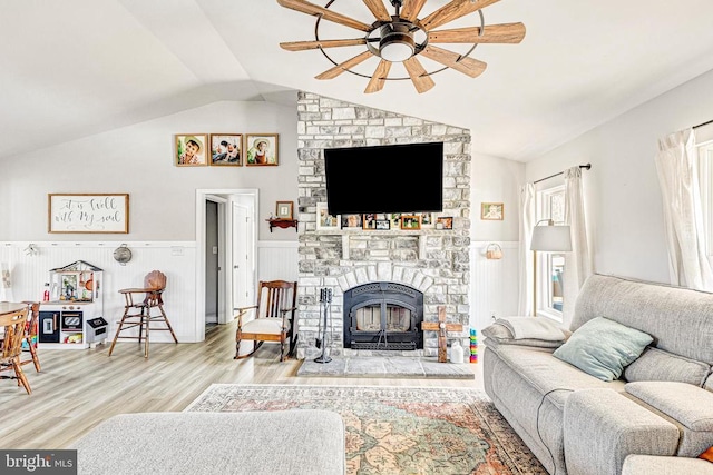 living room with light wood-type flooring, ceiling fan, vaulted ceiling, and a stone fireplace