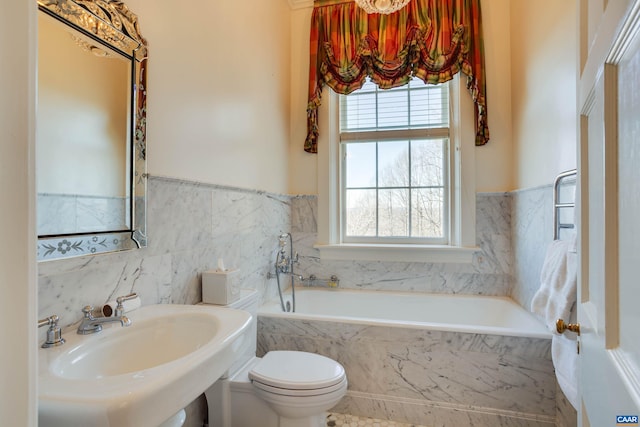 bathroom featuring a garden tub, a sink, toilet, and wainscoting