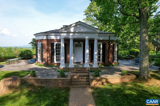 greek revival house with brick siding, covered porch, and a patio