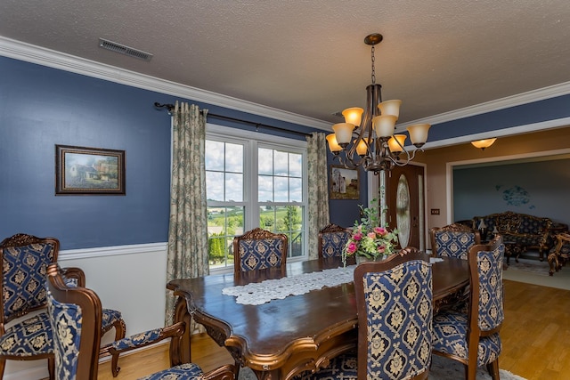 dining space featuring a chandelier, wood finished floors, ornamental molding, and a textured ceiling