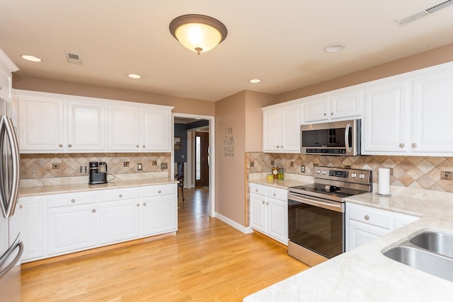 kitchen featuring appliances with stainless steel finishes, backsplash, white cabinetry, light wood-style flooring, and recessed lighting