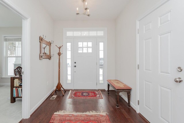 entryway with dark wood-type flooring and an inviting chandelier