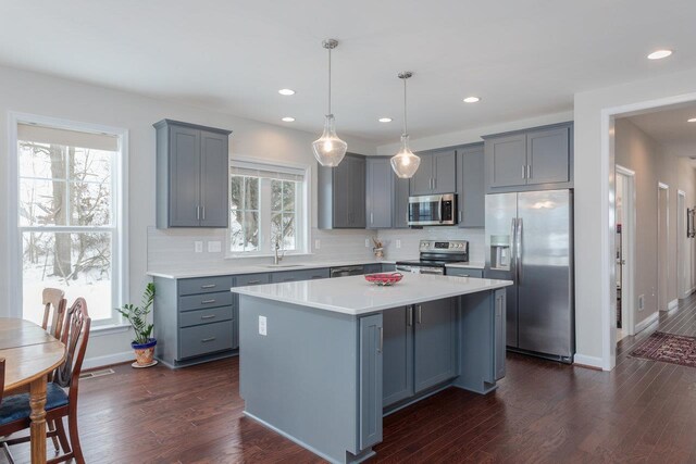 kitchen with sink, hanging light fixtures, stainless steel appliances, a kitchen island, and dark hardwood / wood-style flooring