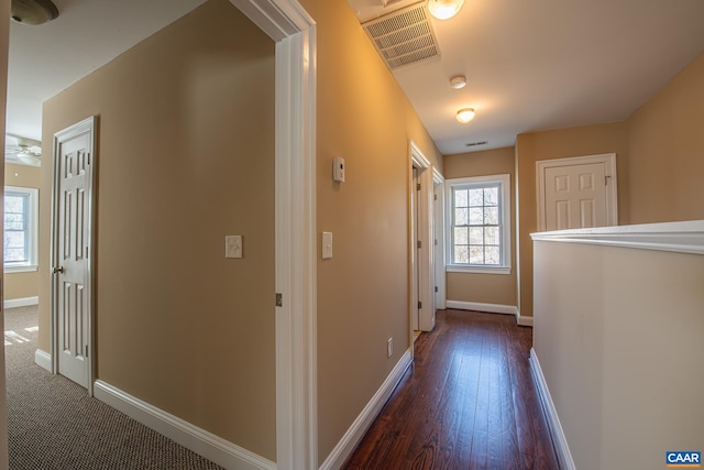 hall featuring visible vents, baseboards, and dark wood-type flooring