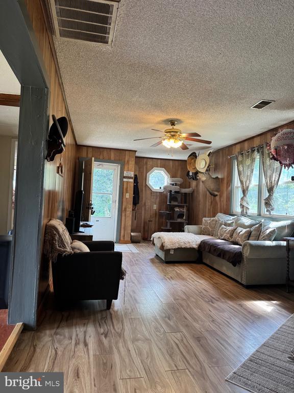 633 Ridge View Ln, Shenandoah, VA 22849 - living area with wooden walls, a textured ceiling, a ceiling fan, and light wood-style flooring