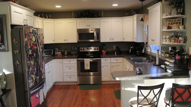 kitchen featuring open shelves, appliances with stainless steel finishes, a sink, wood finished floors, and a peninsula